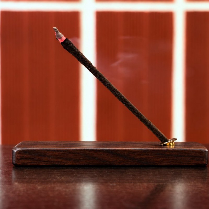 A lit aroma stick resting at 45 degrees in its wooden holder